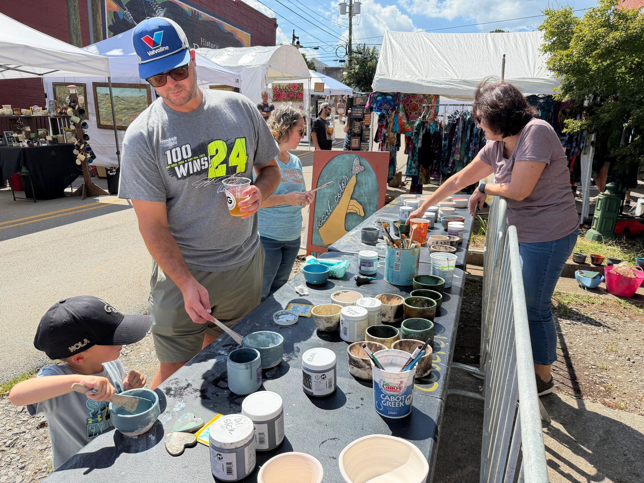 Children painting pottery at an outdoor art festival table