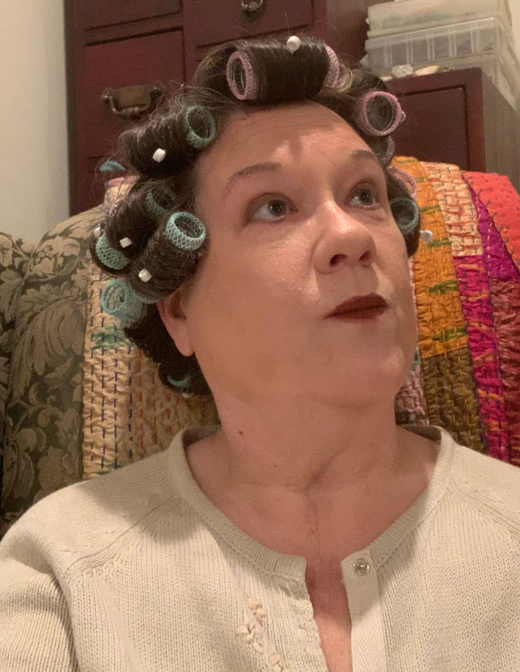 Smiling woman in hair rollers posing in front of colorful artwork